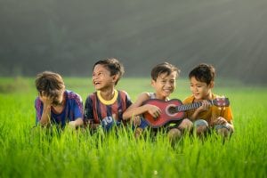 Biographical Information Search Associates ANZ four happy children playing in the grass with one of them playing a ukulele  