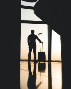 teach abroad Search Associates ANZ silhouette of a man in an airport with his suitcase, watching a plane fly in the air 
