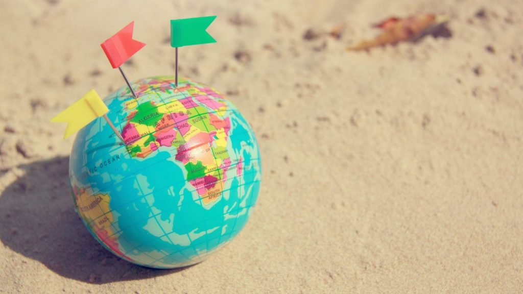 Where can I teach in an international school Search Associates ANZ world globe on the beach with different coloured flags on different parts of the world